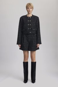 Black and white tweed jacket with buttons, paired with matching shorts. Model wears tall black leather boots. Smooth texture, cropped design.