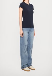 Námorně modré tílko s decentním čtvercovým logem, spárované se světle modrými volně střiženými džíny s grafickým designem na přední straně.