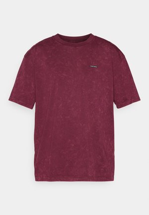 T-shirt de manga curta em bordô, feita de algodão suave com uma textura subtil. Apresenta um pequeno logotipo no lado esquerdo do peito e um design de gola redonda.