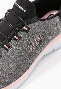 Black and gray athletic shoe with a knitted upper, pink accents, elastic laces, and a white sole featuring a textured grip.
