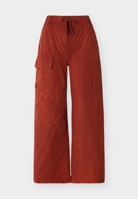 Pantalon à jambes larges couleur rouille avec taille élastique, cordon de serrage, et une poche à rabat sur la cuisse gauche.