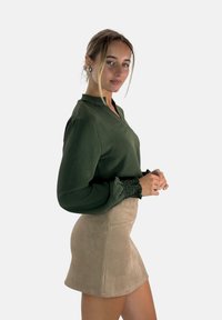 Groene textuur blouse met lange, gepofte mouwen en smockmanchetten, gecombineerd met een beige suède minirok. Eenvoudig ontwerp, neutrale kleuren.