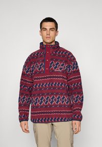 Fleece w kolorze burgundowym z niebieskimi i różowymi wzorami geometrycznymi, z wysokim kołnierzem, zapięciem na zatrzaski oraz małym logo na klatce piersiowej.