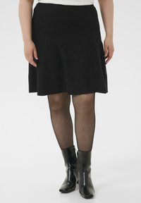 Falda negra acampanada hecha de una tela suave, con una cintura de talle medio. Llevada con medias negras y botines brillantes de punta cuadrada.