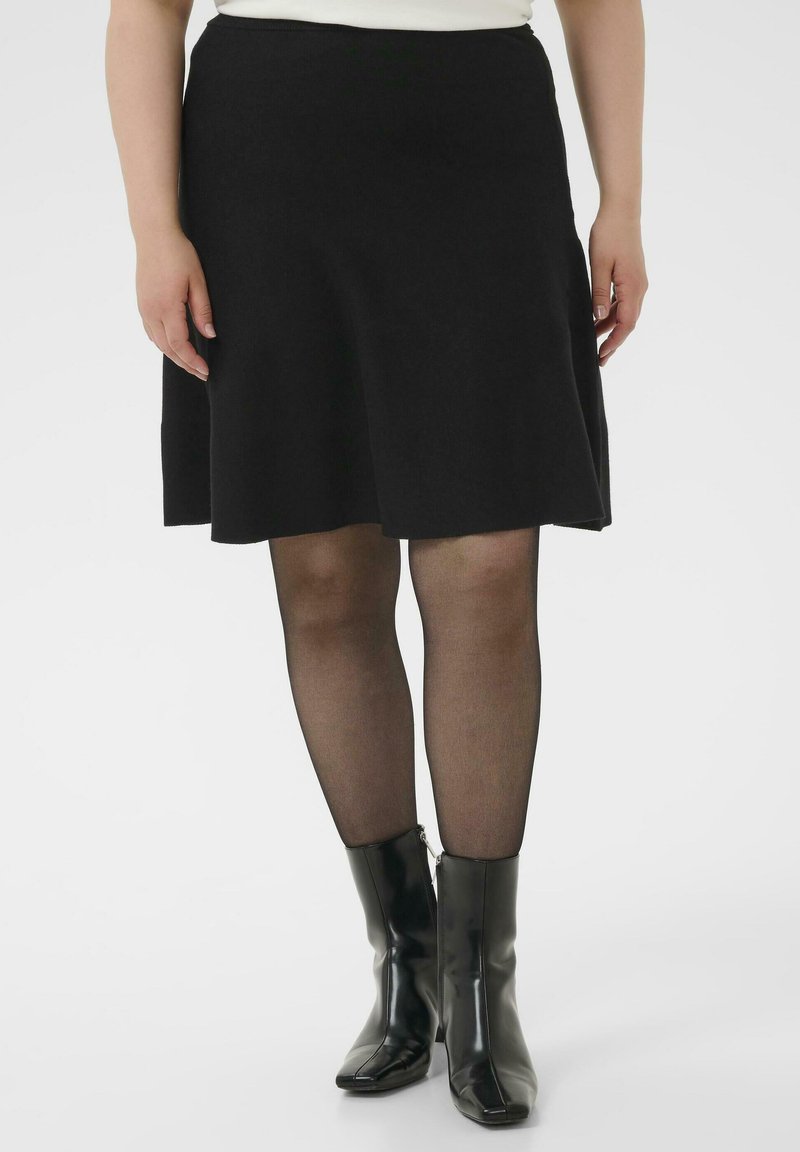 Falda negra acampanada hecha de una tela suave, con una cintura de talle medio. Llevada con medias negras y botines brillantes de punta cuadrada.