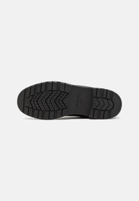 Suela de zapato de goma negra con un patrón de dibujo prominente, que presenta surcos y secciones elevadas para tracción. Marca Geox grabada.