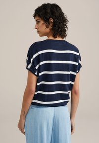 Marinblå randig tröja med vita horisontella ränder, korta ärmar och en avslappnad passform, kombinerad med ljusblå byxor.