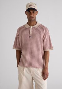Red and beige short-sleeve polo shirt with patterned texture and collar, featuring two buttons and an embroidered logo on the chest.