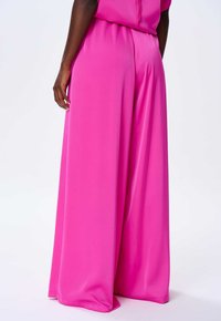 Spodnie z szerokimi nogawkami w jaskrawym różu, wykonane z gładkiego materiału. Posiadają wysoki stan oraz luźny krój, bez widocznych wzorów czy akcentów.