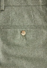 Grüner, strukturierten Stoff mit einem dezenten Muster, ausgestattet mit einem einzelnen Holzknopf und einer rechteckigen Brusttasche mit sauberer Naht.