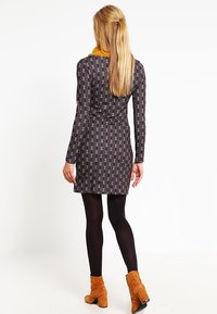 Abito a maniche lunghe con motivo geometrico in nero, bianco e blu, caratterizzato da una silhouette aderente e lunghezza a metà coscia. Indossato con collant scuri e stivali color sabbia.