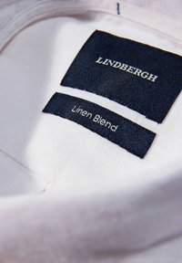 Het linnenmixlabel heeft donkerblauwe tekst op een lichte stofachtergrond met de opschriften "LINDBERGH" en "Linnenmix".