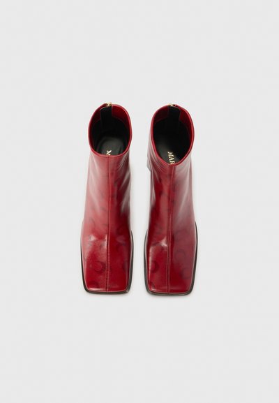 Röda läderankelboots med fyrkantig tå, slät yta och subtilt mönster, med dragkedja på sidan och en liten svart klack.