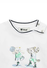 Camiseta de algodón blanca con cuello redondo, que presenta personajes impresos de un oso y un tigre con atuendo de baloncesto, con ribetes en contraste en color marino.