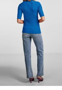 Modrý žebrovaný top s krátkým rukávem, přiléhavý střih, v kombinaci se světle modrými džíny. Modelka nosí fialové podpatky se dekorativním akcentem.