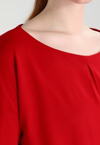 Rode blouse met een brede, off-shoulder halslijn en korte mouwen. Gladde stof met een plooi-detail aan de voorkant, wat zorgt voor een losse pasvorm.