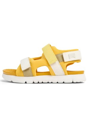 Gul sandal med öppen design, med justerbara kardborreband i vitt och beige, samt en dämpad vit sula med struktur för bra grepp.