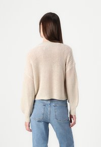 Kremfarget strikket genser med en cropped design, vide ermer, og et strukturert mønster, kombinert med lyseblå høytlivsjeans.