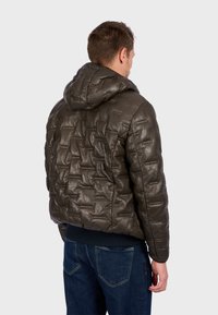 Padded, olive green leather jacket with a hood, featuring a quilted texture and ribbed cuffs, paired with blue denim jeans.