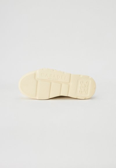 Krém színű sneaker talp, texturált barázdákkal, dombornyomott logóval és sima felülettel. Szintetikus anyagból készült.