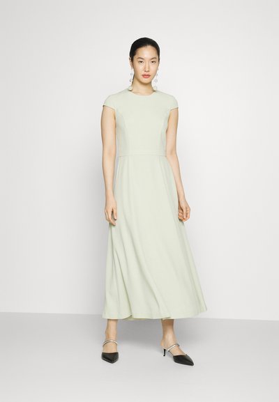 Lichtgroene maxi-jurk met kapmouwen, een aansluitend lijfje en een vloeiende rok. Model draagt zwarte puntige hakken. Eenvoudig ontwerp, geen patronen.