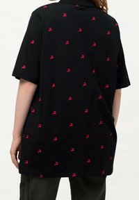 Polo shirt noir à manches courtes avec un motif rouge répété. Fabriqué en tissu doux, il présente une coupe décontractée et un col rabattu.