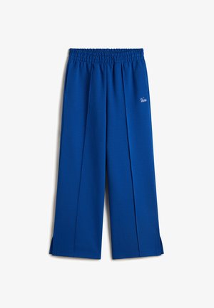 Pantalons larges bleus avec une taille smockée, présentant des plis à l'avant et des fentes latérales à l'ourlet. Tissu doux avec un détail du logo 'Vans'.