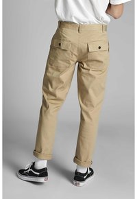 Bežové bavlněné kalhoty s uvolněným střihem, obsahující dvě zadní kapsy a tmavé knoflíky. Ohnuté manžety a doplněné černými teniskami.