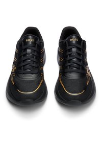 Baskets de sport noires avec empeigne en mesh, accents dorés, design texturé et lacets noirs. Logo « BOSS » sur la languette et les panneaux latéraux.