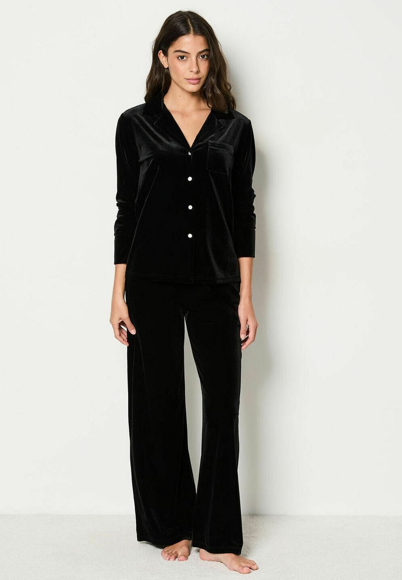 Conjunto de pijama de terciopelo negro con mangas largas, cuello de camisa y botones frontales. Pantalones holgados de corte recto. Textura suave.