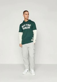Green hoodie with "NEW YORK YANKEES" text, white sleeves, gray cargo pants, and white sneakers. Simple design with casual fit.