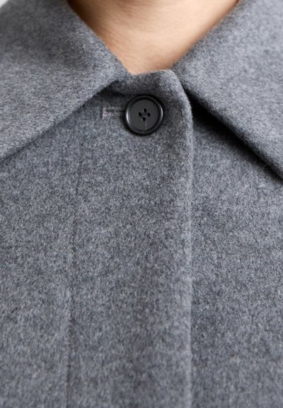 Gray wool coat with a collared neckline, featuring a black button, textured fabric, and visible stitching along the edges.