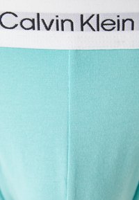 Tessuto di cotone turchese chiaro con una texture a coste; presenta una vita elastica bianca con il logo "Calvin Klein" in lettere nere.