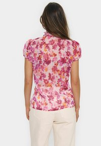 Floral blouse in sheer, lightweight fabric featuring pink and orange flower patterns; short puffed sleeves and a ruffled neckline.
