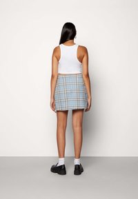 Vit kortärmad tanktop med en blå rutigt minibak. Kjolen har beige och svarta linjer, med en slät textur och en åtsittande design.