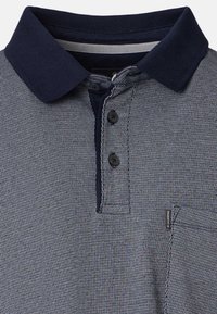 Nahaufnahme eines dunkelblauen Poloshirts mit Muster, festem dunkelblauem Kragen, drei Knöpfen und kleiner Brusttasche mit Markenzeichen.