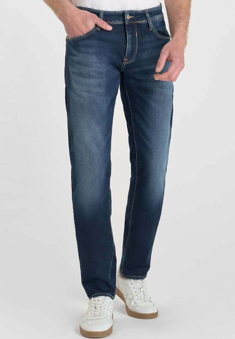 Jeans rectos de color azul oscuro con un acabado deslavado, cinco bolsillos y detalles de costura en naranja, combinados con zapatillas blancas.