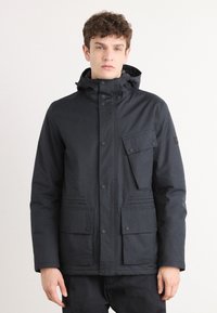 Veste noire imperméable avec un col montant, une capuche réglable et des fermetures à pression. Dispose de multiples poches avant avec une texture lisse et élégante.