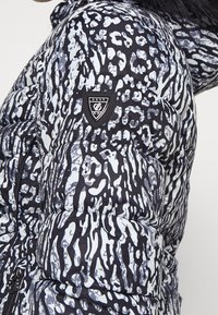 Doudoune noire et blanche avec un motif abstrait, présentant une surface texturée et un écusson logo sur l'épaule.