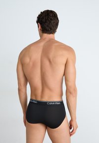 Schwarze Baumwollslips mit einem Logobund, enganliegendem Design, glatter Textur und ohne sichtbare Muster, von hinten gesehen.
