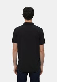 Polo nero, maniche corte, colletto tradizionale, tessuto liscio, taglio dritto, dettagli delle cuciture visibili, indossato con jeans blu scuro.