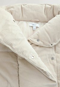 Beige Cordjacke mit gestepptem Design, ausgestattet mit einem doppelt geknöpften Kragen, Druckknöpfen und einem weichen, leichten Futter. Markentag sichtbar.