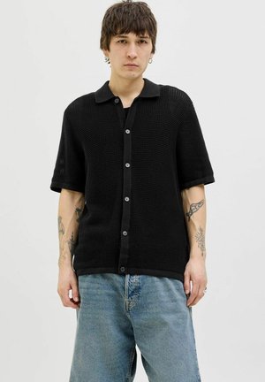 Black short-sleeve shirt with a textured, waffle-knit fabric, featuring a collared neckline and buttons down the front. Loose fit.