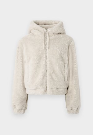 Felpa corta con zip in pile, di colore beige chiaro. Presenta un cappuccio, polsini elasticizzati e due tasche laterali. Texture morbida con un look accogliente.