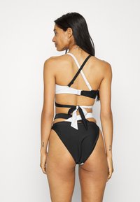 Biquíni de duas peças em preto e branco com costas abertas e laços, alças ajustáveis e um design de parte inferior alta.
