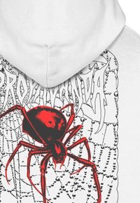 Felpa bianca con una grafica di ragno rossa. Il ragno presenta un aspetto lucido, posizionato su uno sfondo di rete in bianco e nero a contrasto.