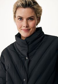 Schwarze Steppjacke mit hohem Kragen, die mit diagonalen Nähten und zwei sichtbaren schwarzen Knöpfen versehen ist. Weicher Textur und isoliertes Design.