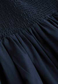Robe bleu marine avec un corsage froncé et une jupe évasée plissée, confectionnée dans un tissu doux, présentant une texture lisse et un design structuré.