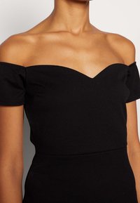 Vestido negro sin mangas con un corpiño ajustado, que presenta un amplio escote corazón y una tela texturizada. Acabado liso, sin estampados.