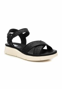 Sandalias negras con correas texturizadas, hebilla ajustable y suela blanca ligera. Diseño de punta abierta con patrón de correas en diagonal.